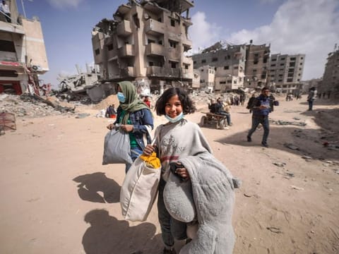 Displaced Palestinians carry their belongings through a street near the rubble of houses destroyed by Israeli bombardment in Khan Younis in the southern Gaza Strip on March 6, 2024.