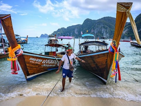 Picture shows a sailor walking in front of long tail boats moored on a beach on Phi Phi Don island in Thailand.