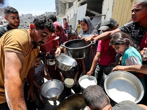 Palestinians gather to receive food cooked by a charity kitchen near houses destroyed in the Israeli military offensive, in Khan Younis in the southern Gaza Strip, May 30, 2024.