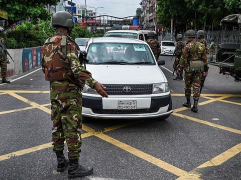 Commuters move along the road as Bangladesh soldiers stand guard following a curfew and the deployment of military forces in Dhaka.