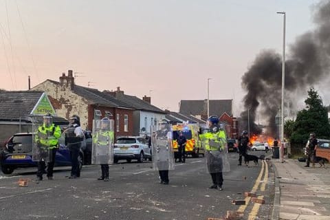 Smoke billows from a fire started by protesters as riot police stand guard after disturbances near the Southport Islamic Society Mosque in Southport, northwest England, on July 30, 2024, a day after a deadly child knife attack.