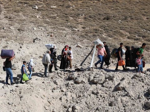 People fleeing Israeli bombardment in Lebanon, walk around a crater caused by an Israeli strike, in the area of Masnaa on the Lebanese side of the border crossing with Syria, on October 4, 2024.