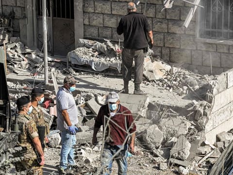 Lebanese army soldiers stand by as people clear debris and rubble from the site of a previous Israeli air strike on the village of Aito in northern Lebanon on October 15, 2024.