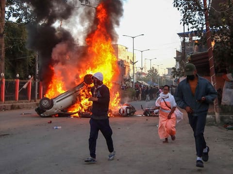 People run past burning vehicles of India's Bharatiya Janata Party (BJP) MLA during a protest to condemn the alleged killing of women and children in Imphal, capital of India's violence-hit northeastern state of Manipur on November 16, 2024.