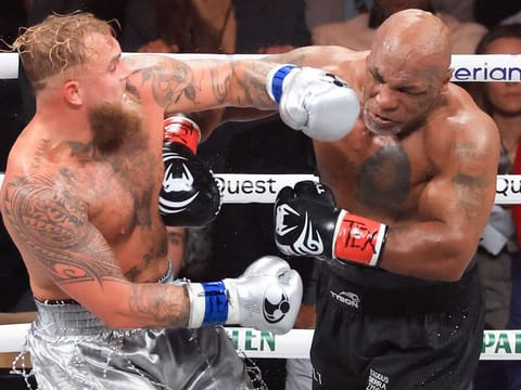 Jake Paul (L) punches Mike Tyson during their heavyweight bout at AT&T Stadium on November 15, 2024 in Arlington, Texas.