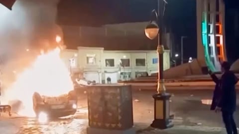A man is shown holding a device to document burning vehicles during a night of mass protests in Zanjan, Iran