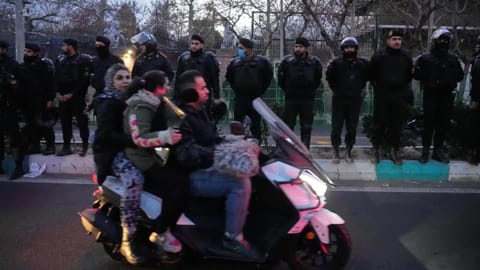 Policemen protect the British Embassy during a protest by hardline supporters of the Iranian government, as people ride on their motorbike in Tehran, Iran