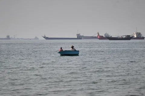 Two men sit in a small boat on the water as a mix of bulk carriers, cargo ships, and service vessels line the horizon in the Strait of Hormuz off Bandar Abbas, Iran, Monday, April 27, 2026.(Razieh
Poudat/ISNA via AP)