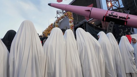 A group of girls stand beside a “Khaybar-buster” missile during a mass wedding ceremony 