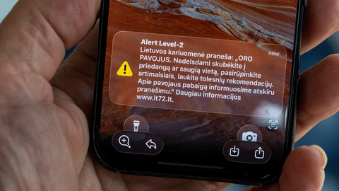 The phone shows the received message "The Lithuanian military reports: "AIR DANGER. Hurry to cover or a safe place without delay, take care of your loved ones, wart for further recommendations''