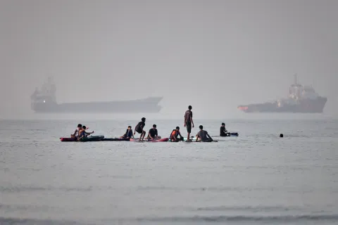 People gather on paddleboards in shallow water as cargo and service vessels are anchored in the Strait of Hormuz off Bandar Abbas, Iran, Monday, June 1, 2026
