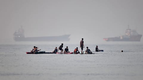 People gather on paddleboards in shallow water as cargo and service vessels are anchored in the Strait of Hormuz off Bandar Abbas, Iran