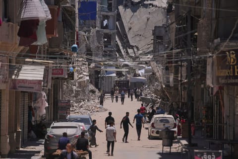 Palestinians walk along a street surrounded by buildings destroyed by Israeli military strikes in Khan Younis, southern Gaza Strip on May 29.