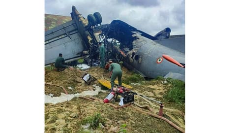 Security personnel and others stand near damaged remains of a transport aircraft of the Indian Air Force (IAF) that crashed while landing, in Jorhat district, Assam