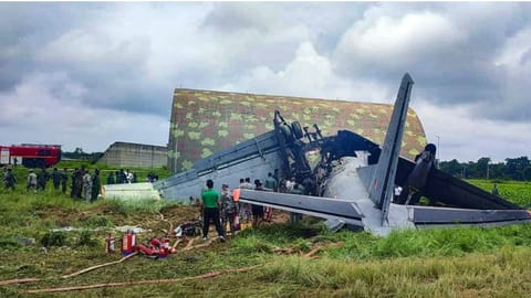 Security personnel and others stand near damaged remains of a transport aircraft of the Indian Air Force (IAF) that crashed while landing, in Jorhat district, Assam
