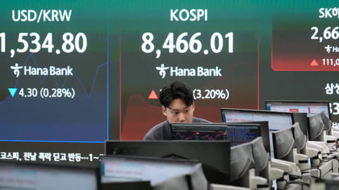 A currency trader watches monitors near a screen showing the Korea Composite Stock Price Index