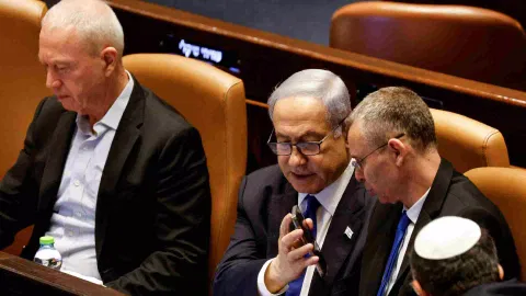 Israeli Prime Minister Benjamin Netanyahu shows Justice Minister Yariv Levin his phone as lawmakers gather at the Knesset plenum to vote on a bill that would limit some Supreme Court power, in Jerusalem