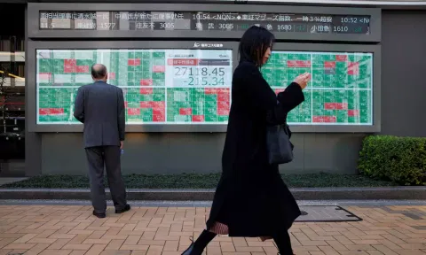 A woman walks past a man examining an electronic board showing Japan's Nikkei average and stock quotations outside a brokerage (Reuters)