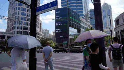 Pedestrians wait to cross a road at a junction near a giant display of stock indexes in Shanghai (Photo/Reuters)
