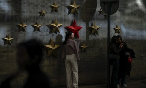 A beam of sunlight is cast on a woman as visitors take souvenir photos with the communist symbol of stars on display along a street in Beijing (AP)