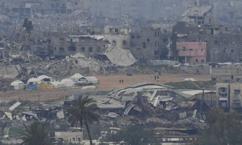 Palestinians are seen near destroyed buildings by Israeli bombardments inside the northern Gaza Strip as seen from southern Israel (AP)