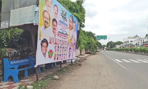 Commuters wait on road, as banner welcoming EPS hides bus stop