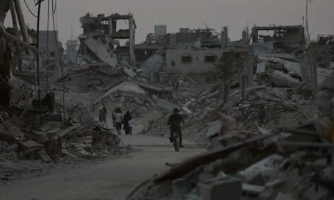 Displaced Palestinians walk among the ruins of destroyed buildings in Khan Younis, Gaza Strip (AP)