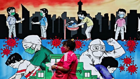 A woman wearing a protective face mask walks past a mural promoting awareness of the coronavirus disease