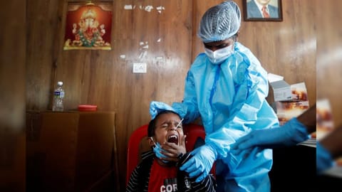 A health worker in personal protective equipment (PPE) collects a swab sample from a child