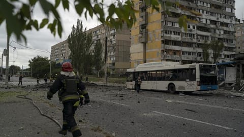 Firefighters and police officers work on a site where an explosion created a crater on the street
