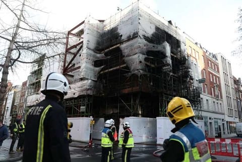 Firefighters look at the damaged caused by a fire at a construction site in central London