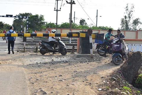 Two-wheeler riders crossing the railway gate in Annanur while it is closed for a train to pass