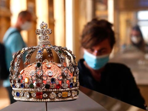 A visitor wearing face mask stands in front of the Crown of Louis XV held in the Apollo gallery at the Louvre Museum in Paris.
