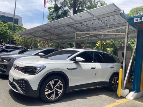 An EV charging station topped by solar panels inside the Department of Energy compound in Taguig, Manila, where VW and BYD vehicles are parked.
