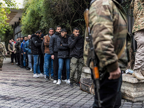 A member of Syria's transitional government security forces stands guard as former soldiers, police members, and civilians queue up at a centre for handing over small arms and security registration with the new authorities in Damascus on December 24, 2024. 