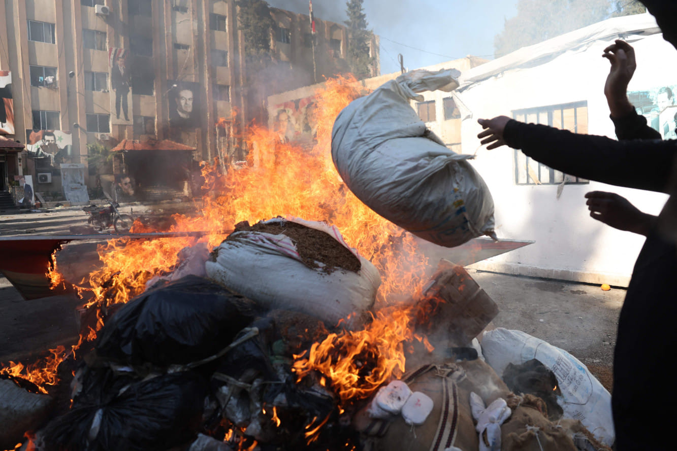 A man throws a bag onto a pile of burning illicit drugs, as Syria's new authorities burn drugs reportedly seized from a security branch, in Damascus on December 25, 2024.  
