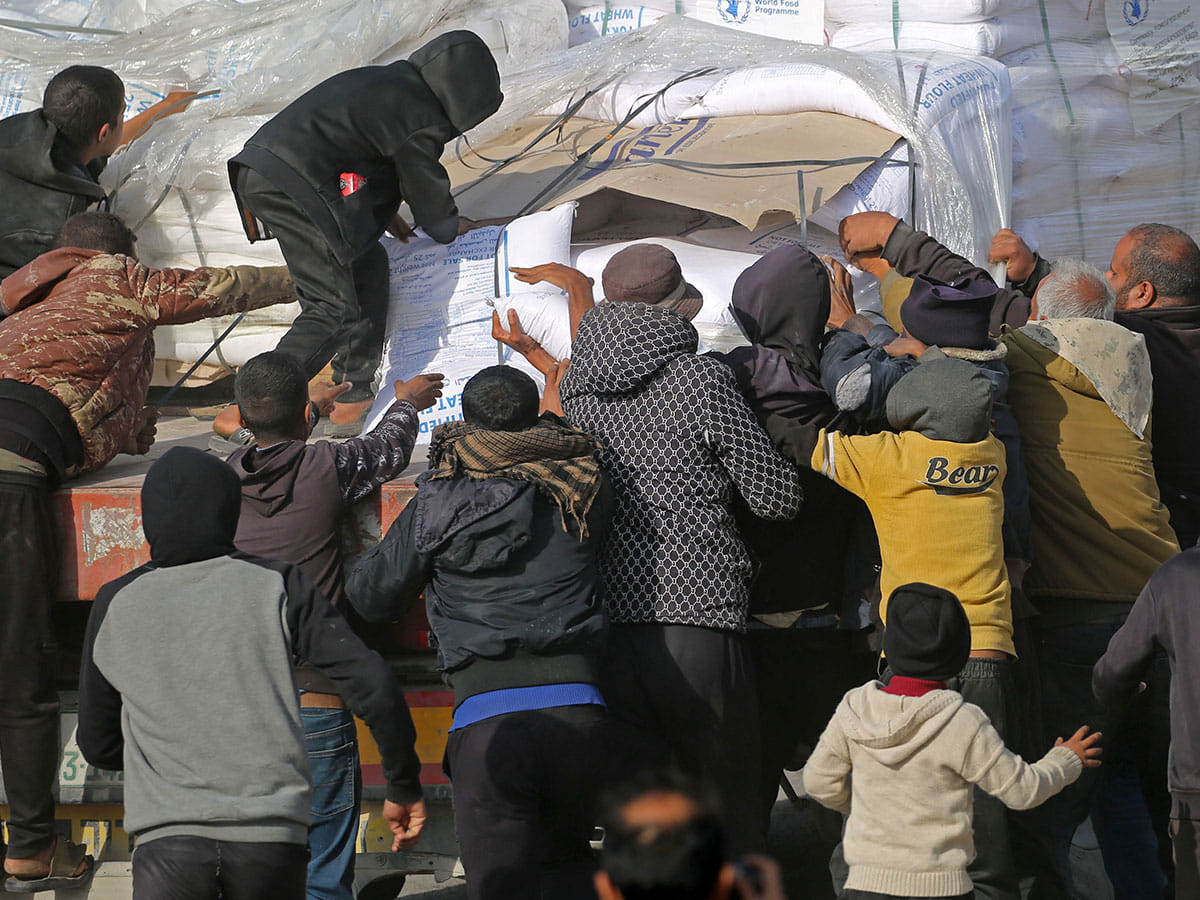 People gather to collect humanitarian aid after trucks arrived in the Gaza Strip via the Kerem Shalom crossing, also known as Karem Abu Salem, on January 19, 2025.  