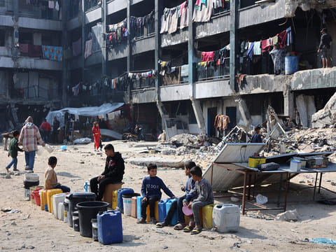 Palestinian children sit and wait next to water cans at a school turned shelter in Jabalia in the northern Gaza Strip on February 4, 2025.  