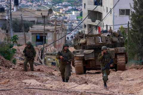 Israeli soldiers walk behind a tank at the Jenin camp for Palestinian refugees in the occupied West Bank during a military operation on February 24, 2025. 