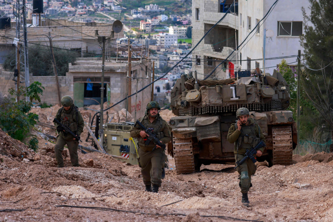Israeli soldiers walk behind a tank at the Jenin camp for Palestinian refugees in the occupied West Bank during a military operation on February 24, 2025. 