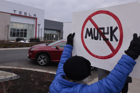 A person holds up a sign during a protest against Elon Musk outside of a Tesla dealership in West Bloomfield, Michigan, on February 27, 2025.