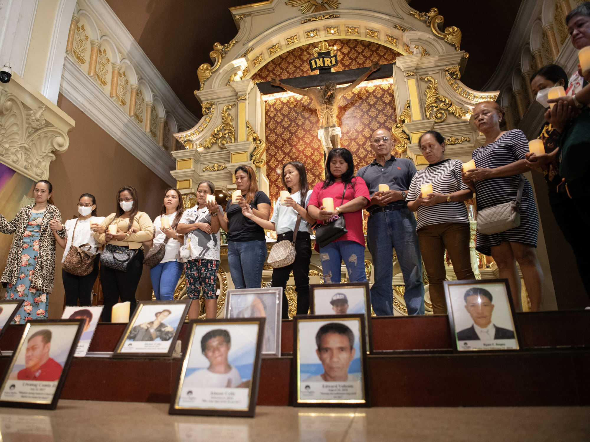 Relatives of victims of former Philippine president Rodrigo Duterte's war on drugs join hands in front of portraits of their deceased loved ones as they hold lit candles during a mass at a church in Manila on March 11, 2025.
