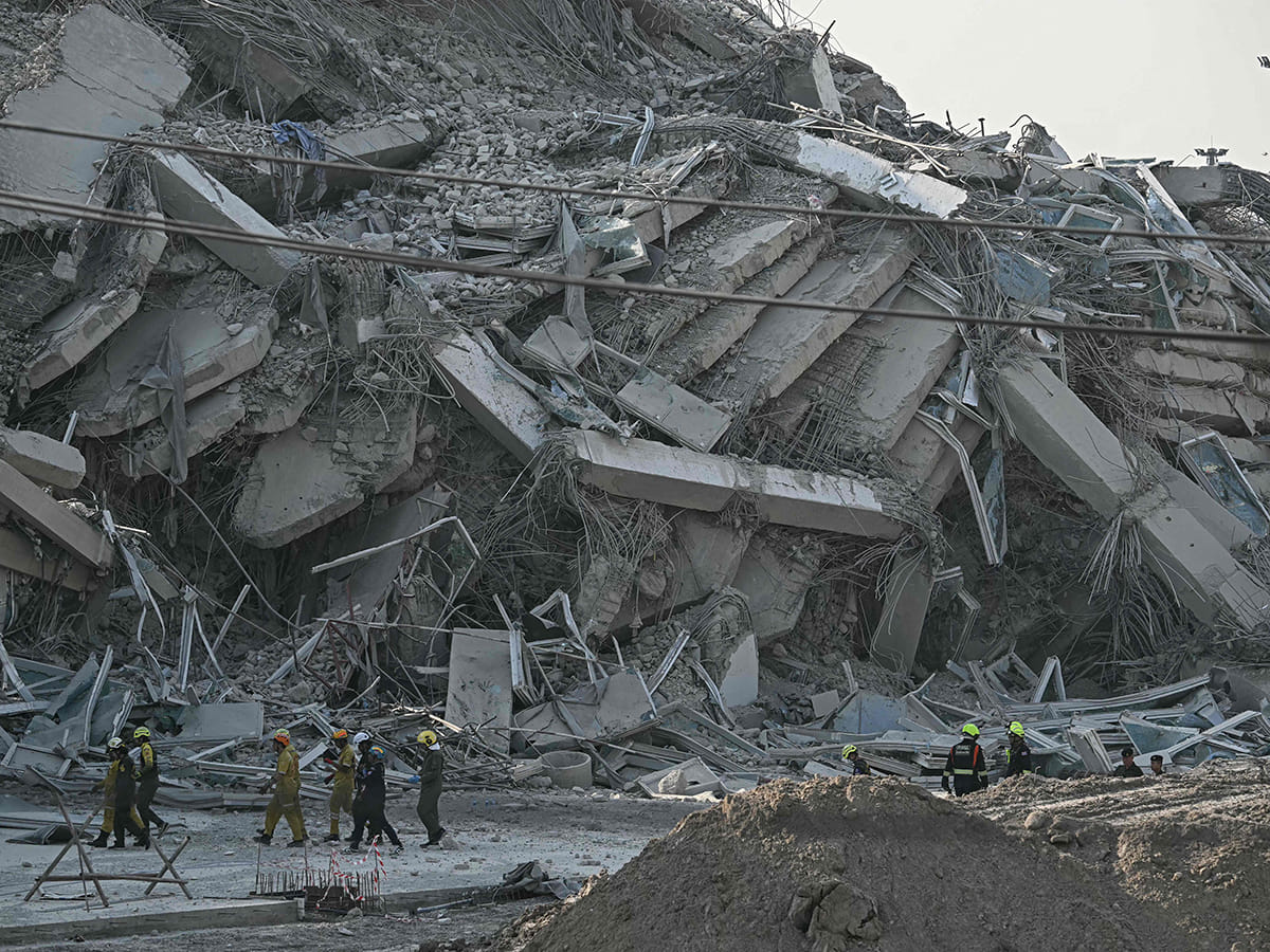 Rescue workers walk past debris of a construction site after a building collapsed in Bangkok on March 28, 2025, following an earthquake. 