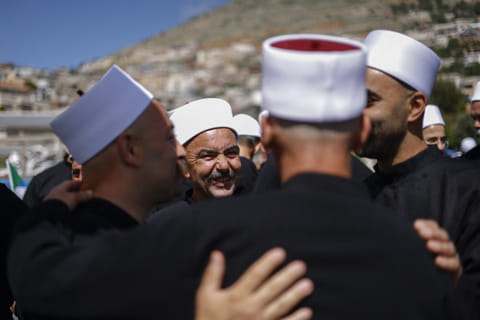 Druze clerics welcome visitng counterparts who just arrived from Syria in a bus through a border barrier guarded by Israeli soldiers, in the village of Majdal Shams in the Israeli-annexed Golan Heights, on April 25, 2025.