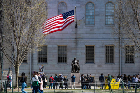 Demonstrators with signs stand around the John Harvard Statue following a rally against President Donald Trumps attacks on Harvard University at the university in Cambridge, Massachusetts, on April 17, 2025.  