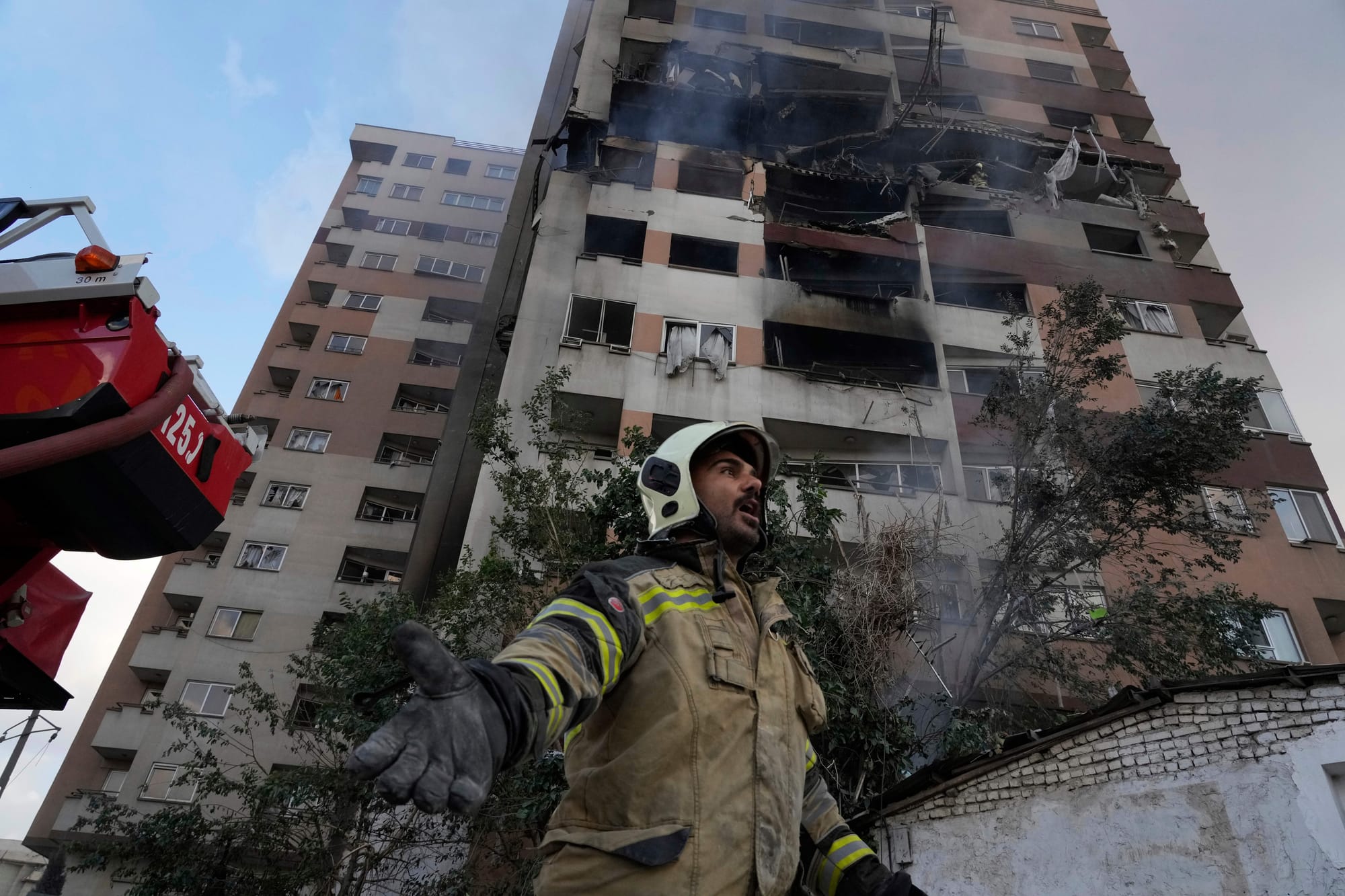 A firefighter calls out his colleagues at the scene of an explosion in a residence compound in northern Tehran, Iran, Friday, June 13, 2025.