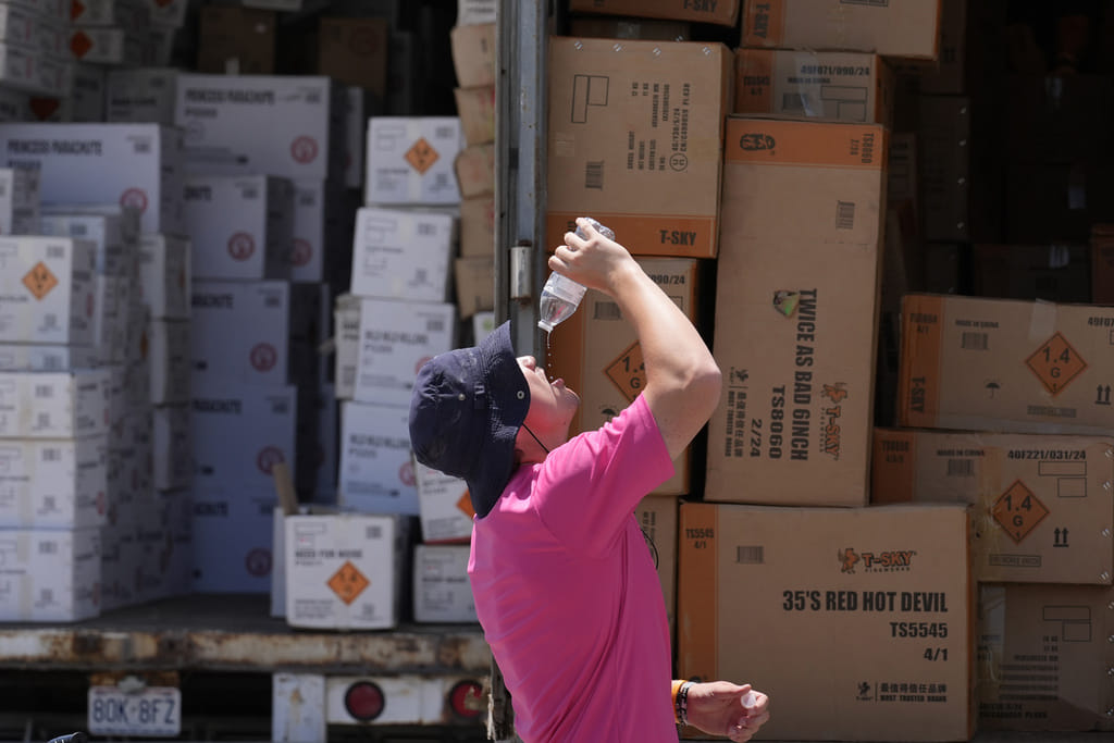 Wyatt Seymore pours the last drops of liquid from a water bottle into his mouth as he takes a break from unloading a stiflingly hot trailer of fireworks outside Powder Monkey Fireworks ahead of the opening of the stand, June 17, 2024, in Weldon Spring, Missouri.  