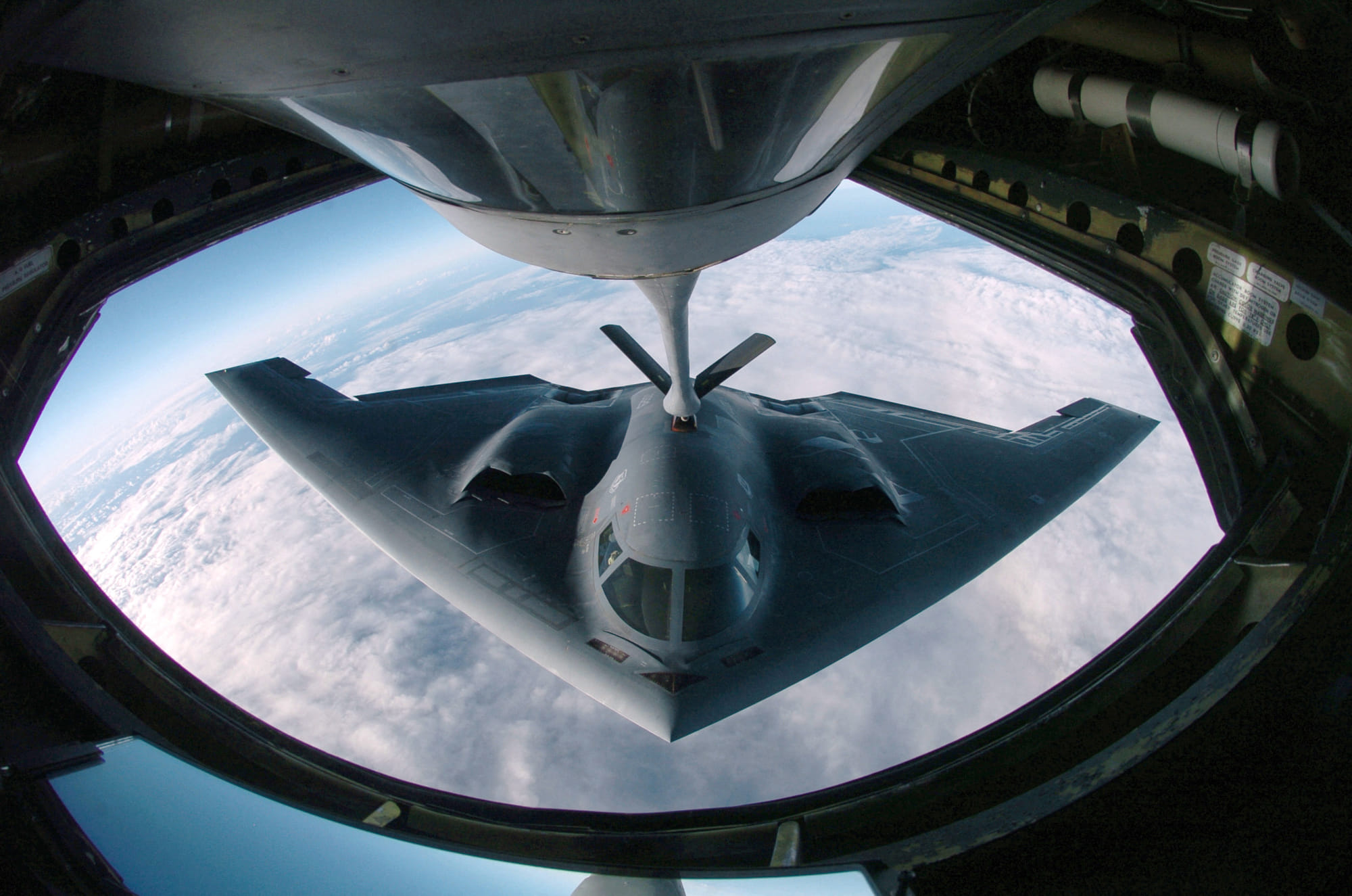 A B-2 Spirit multi-role bomber conducting air refueling operations with a KC-135 Stratotanker over the Pacific Ocean.