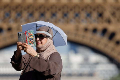 A tourist uses a small umbrella hat to protect herself from the sun during a heatwave at the Trocadero square near the Eiffel Tower, in Paris, on June 30, 2025.
