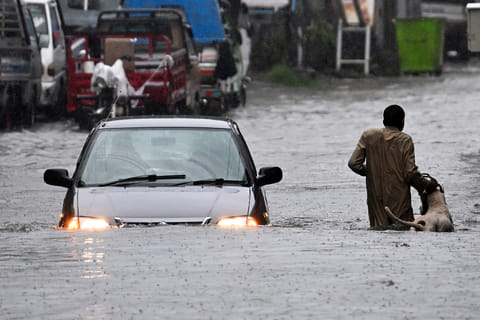 A man along with his dog while a car wade through a flooded street during heavy monsoon rains in Rawalpindi on July 17, 2025.